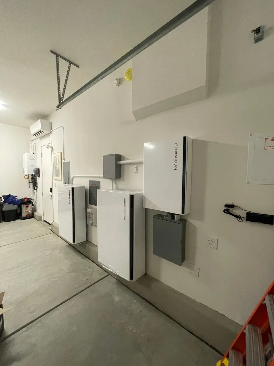 Two Franklin batteries and a run of subpanels and disconnects along the length of a garage wall.