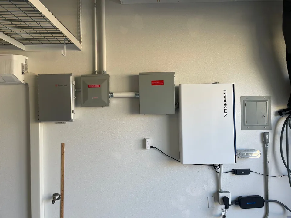 A Franklin control unit beside Enphase equipment, electrical panels, and surface-mounted conduit in a garage.