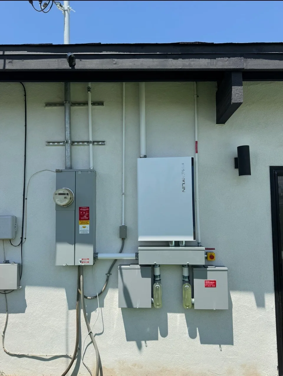 A Franklin battery mounted on an exterior wall between a meter panel and a pair of fused disconnects.