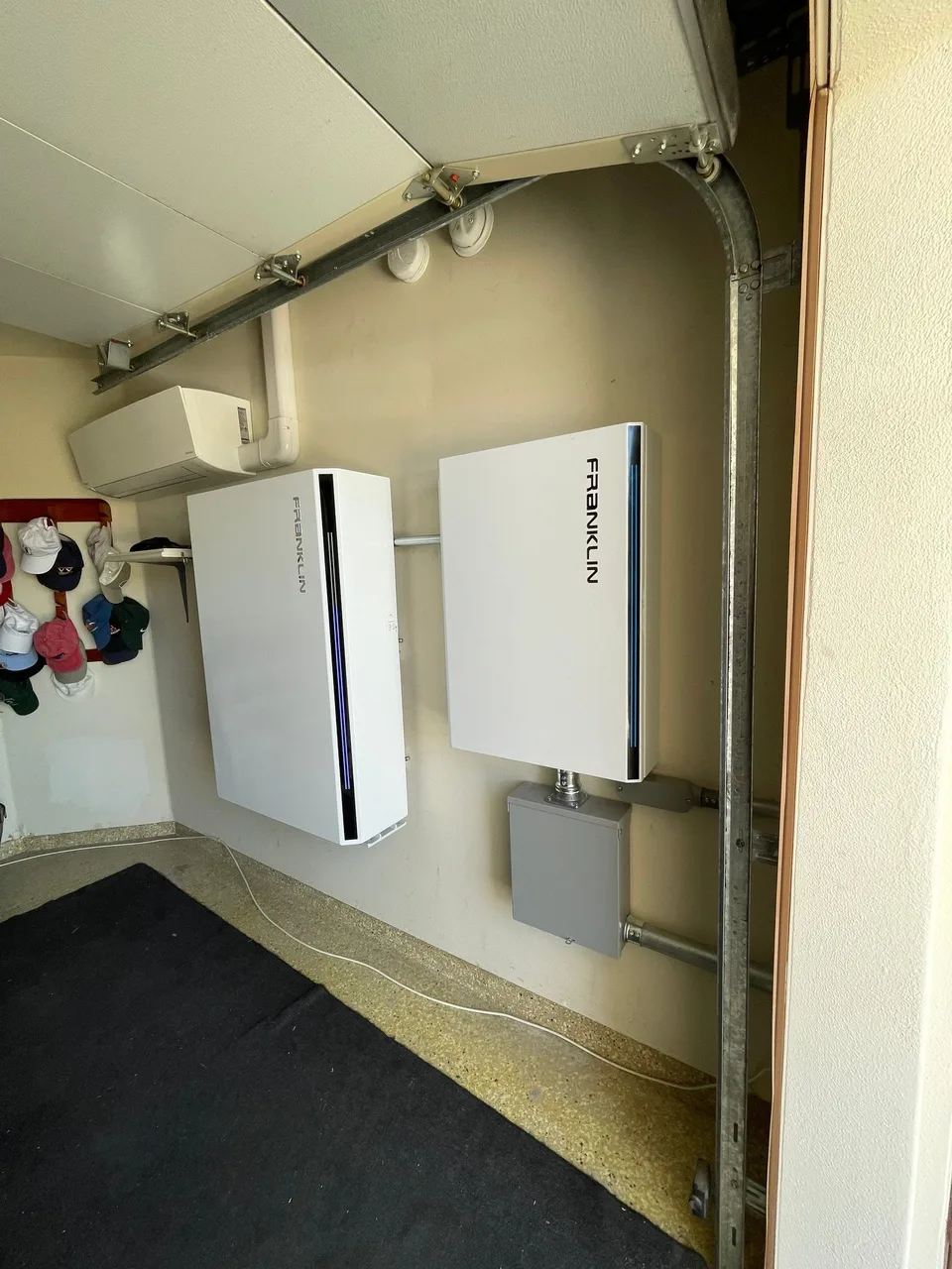 Two wall-mounted Franklin batteries beside a garage opening, with a control enclosure below and a mini-split above.